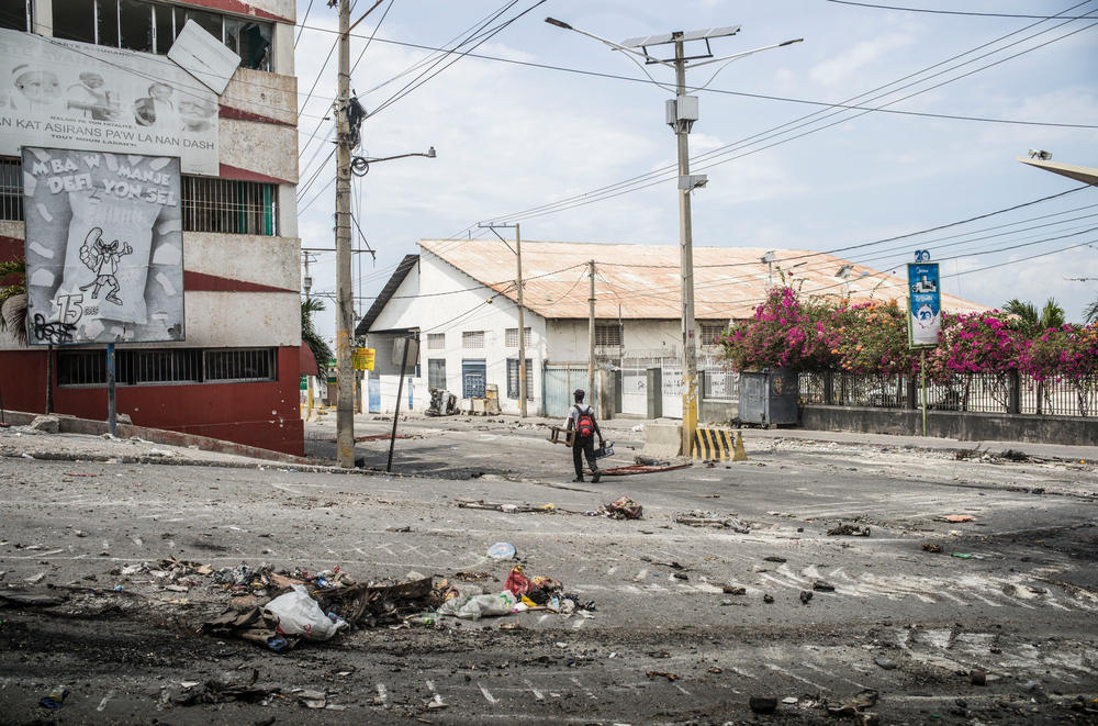 Ein Mensch läuft allein auf einer Straße, neben ihm Spuren der Zerstörung und Gewalt.