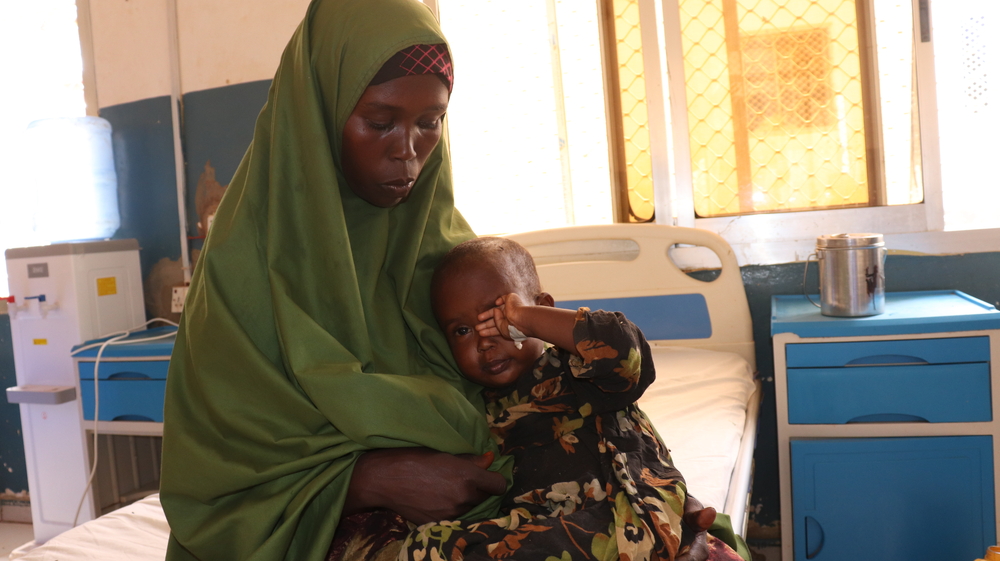 Foto von dem Kleinkind Saidya im Arm ihrer Mutter. Die Mutter blickt ernst auf ihre Tochter herab, während sich Saidya gerade ein Auge reibt