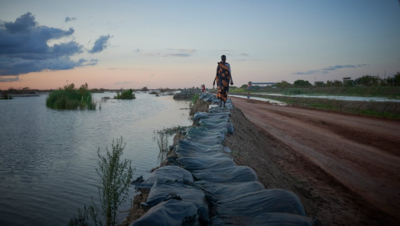 Frau läuft im Südsudan einen Deich enlang - Flutwasser ist überall.
