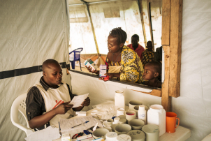 A woman and child talk discuss medications with a seated health care worker.