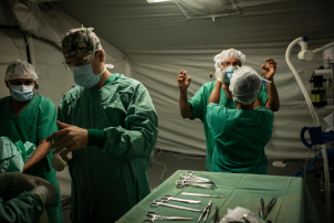 Five doctors help each other prepare their protective equipment in an operating room