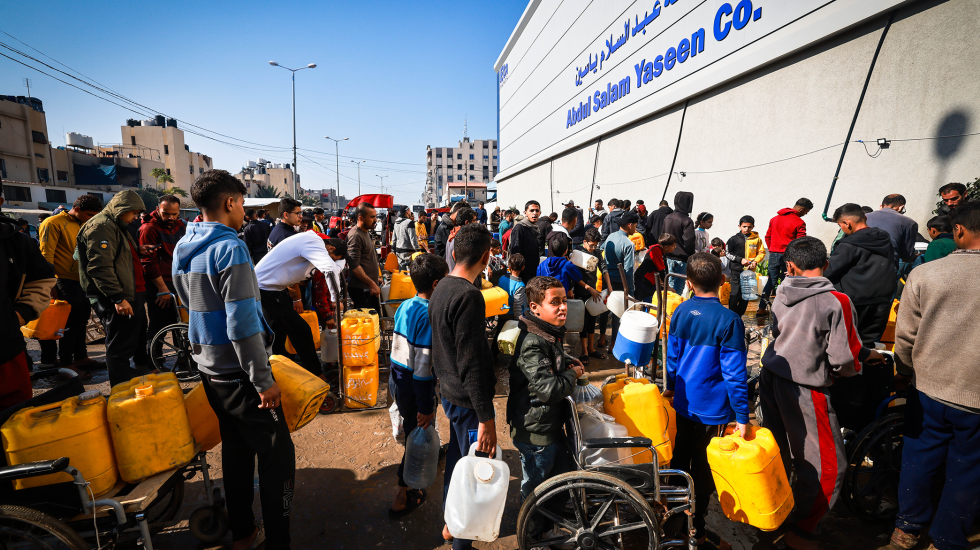 Gruppe vertriebener Menschen steht mit Wassercontainern an