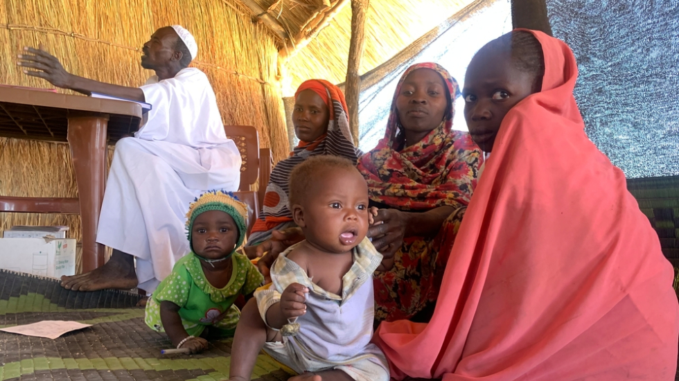Mütter sitzen mit ihren Kindern in einer Hütte auf dem Boden und warten auf eine medizinische Untersuchung.