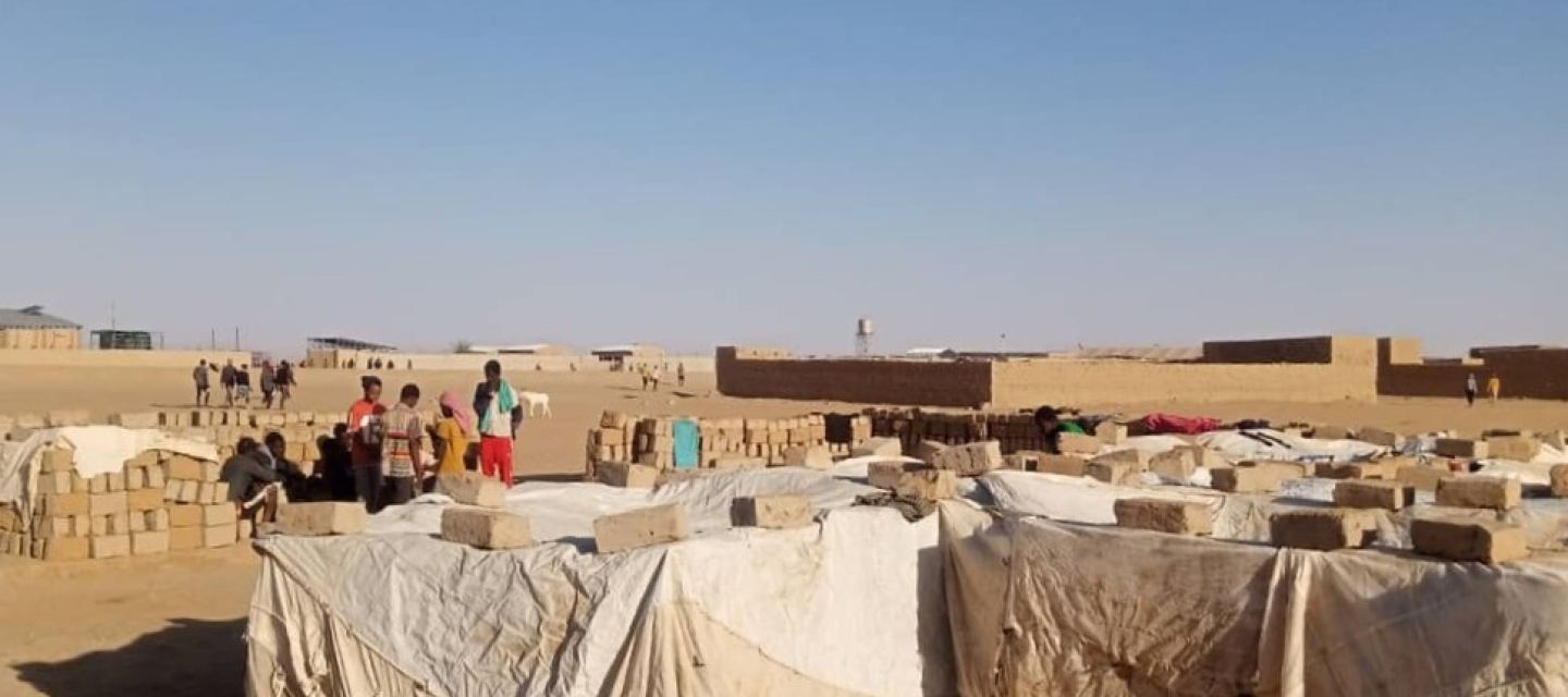 Menschen stehen in der Wüste Nigers auf einer offenen Fläche mit provisorischer Behausung.